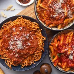 Pyszny obiad bez mięsa: spaghetti i penne w sosie pomidorowym, posypane parmezanem. Obok bagietka i pomidorki.