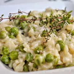 Kremowe risotto z groszkiem, posypane parmezanem i udekorowane gałązką tymianku. Pyszne danie, które zachwyca smakiem.