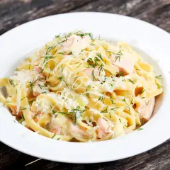 Pyszny makaron z łososiem w kremowym sosie, posypany parmezanem i świeżym koperkiem. Idealny na szybki obiad.
