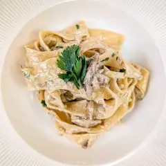 Pappardelle z kremowym sosem i kawałkami grzybów, udekorowane natką pietruszki. Pyszny makaron z grzybami.