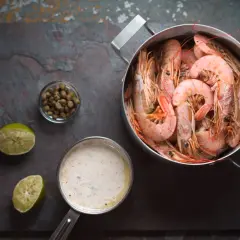 Gotowane krewetki w garnku, obok sos, kapary i limonki. Idealne do przygotowania krewetek gotowanych.