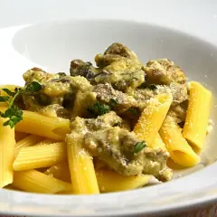 Penne z kremowym sosem i kawałkami wołowiny, posypane parmezanem i udekorowane gałązką ziół. Pyszny makaron z wołowiną.
