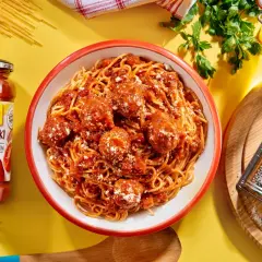 Pyszne spaghetti bolognese z klopsikami w sosie pomidorowym, obok słoik sosu i tarka z parmezanem.