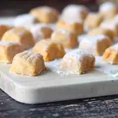 Pomarańczowe gnocchi z dyni, posypane cukrem pudrem, ułożone na desce.