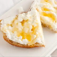 Dwa kawałki chleba z obficie rozsmarowanym twarogiem i polane miodem. Idealny twaróg na śniadanie.