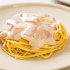 Pyszny makaron z jajkiem i boczkiem w kremowym sosie, posypany pieprzem, podany na białym talerzu.