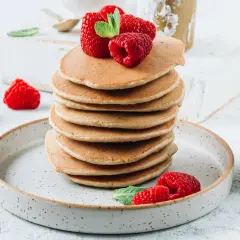 Stos fit pancakes z odżywki białkowej bez banana, udekorowane malinami i miętą, na talerzu.