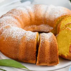 Puszysta babka piaskowa, oprószona cukrem pudrem, z pomarańczami w tle. Idealna na deser.