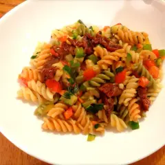Kolorowy makaron fusilli z suszonymi pomidorami, cukinią, papryką i natką pietruszki. Pyszny makaron z warzywami na białym talerzu.