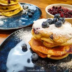 Pyszne pancakes z borówkami, posypane cukrem pudrem i świeżymi owocami. Idealne na śniadanie.