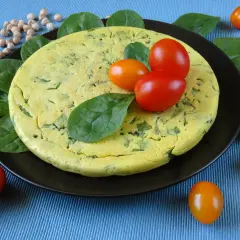 Puszysty omlet z ciecierzycy ze szpinakiem, ozdobiony pomidorkami koktajlowymi i świeżym szpinakiem.