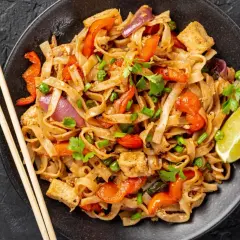 Pyszny pad thai z kurczakiem, warzywami i makaronem ryżowym, udekorowany kolendrą i ćwiartką limonki.