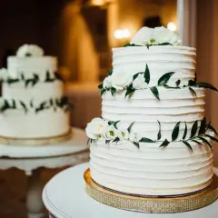 Elegancki tort piętrowy na stelażu, ozdobiony białymi różami i zielonymi liśćmi. Idealny pomysł, jak zrobić tort piętrowy na stelażu na specjalną okazję.