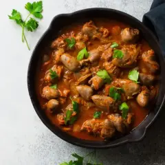 Gulasz z serc drobiowych w sosie pomidorowym, udekorowany natką pietruszki, podany w żeliwnej patelni.