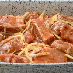 Surowe żeberka pieczone w marynacie z cebulą i przyprawami, gotowe do pieczenia.