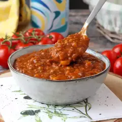 Miseczka sosu bolońskiego z pomidorami w tle.