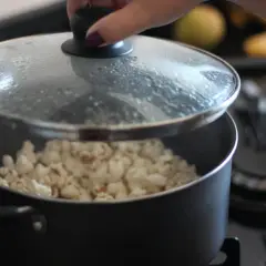 Ręka podnosi pokrywkę garnka, spod której widać gotowy popcorn. Tak właśnie robi się popcorn w garnku!