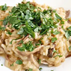 Kremowe risotto z grzybami, posypane świeżą natką pietruszki. Idealne danie dla miłośników leśnych smaków.