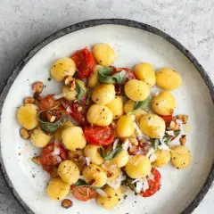 Pyszne gnocchi z pomidorkami koktajlowymi, orzechami i szałwią. Danie posypane parmezanem.