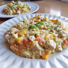 Pyszne risotto z kurczakiem, papryką i ziołami, udekorowane listkiem bazylii. Idealne na obiad.