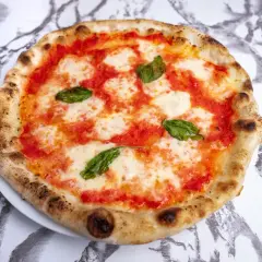 Pyszne ciasto na pizzę neapolitańską, z sosem pomidorowym, mozzarellą i listkami bazylii, na marmurowym tle.