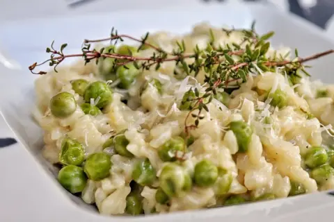 Kremowe risotto z groszkiem, posypane parmezanem i udekorowane gałązką tymianku. Pyszne danie, które zachwyca smakiem.