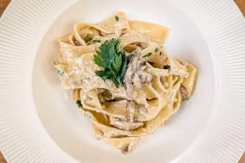 Pappardelle z kremowym sosem i kawałkami grzybów, udekorowane natką pietruszki. Pyszny makaron z grzybami.