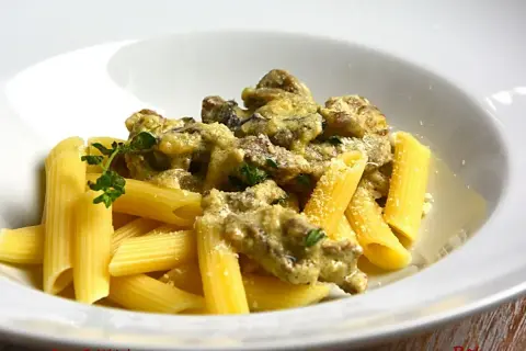 Penne z kremowym sosem i kawałkami wołowiny, posypane parmezanem i udekorowane gałązką ziół. Pyszny makaron z wołowiną.