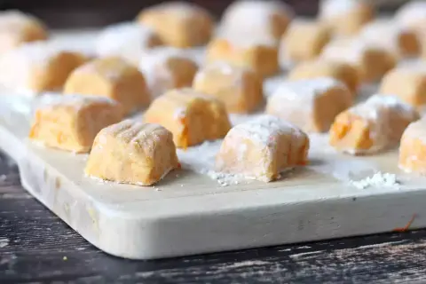 Pomarańczowe gnocchi z dyni, posypane cukrem pudrem, ułożone na desce.