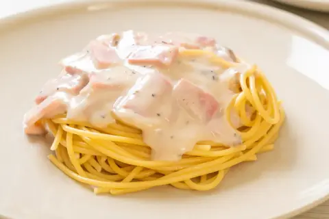 Pyszny makaron z jajkiem i boczkiem w kremowym sosie, posypany pieprzem, podany na białym talerzu.
