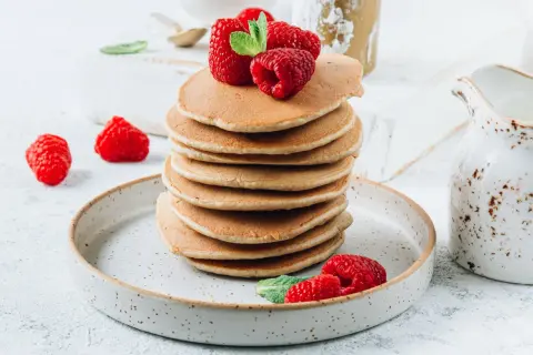 Stos fit pancakes z odżywki białkowej bez banana, udekorowane malinami i miętą, na talerzu.