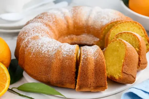 Puszysta babka piaskowa, oprószona cukrem pudrem, z pomarańczami w tle. Idealna na deser.