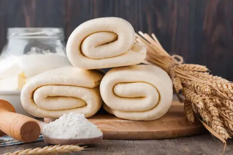 Rolowane ciasto francuskie, choć po terminie, wygląda apetycznie. Obok kłosy zbóż i mąka.