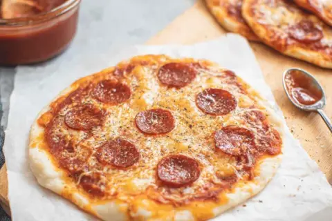 Pyszna pizza z tortilli z pepperoni i serem, obok sos w miseczce i łyżeczka.