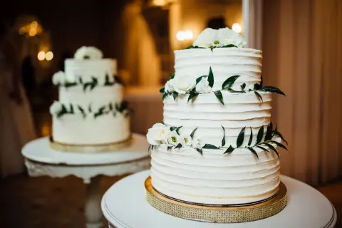 Elegancki tort piętrowy na stelażu, ozdobiony białymi różami i zielonymi liśćmi. Idealny pomysł, jak zrobić tort piętrowy na stelażu na specjalną okazję.