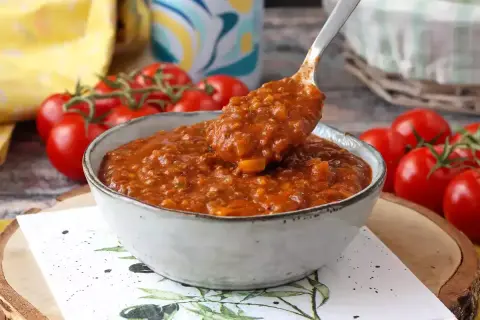 Miseczka sosu bolońskiego z pomidorami w tle.