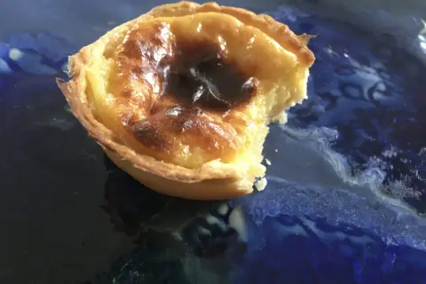 Pyszne, lekko przypalone pastel de nata na niebieskim talerzu. Kruche ciasto i kremowe nadzienie.