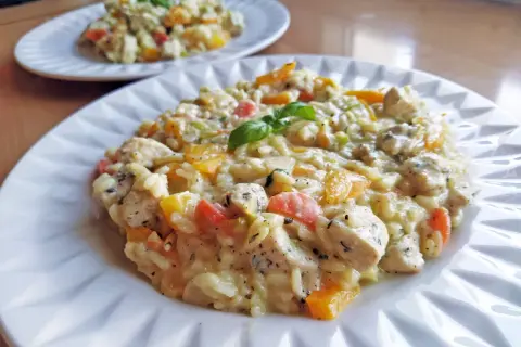 Pyszne risotto z kurczakiem, papryką i ziołami, udekorowane listkiem bazylii. Idealne na obiad.