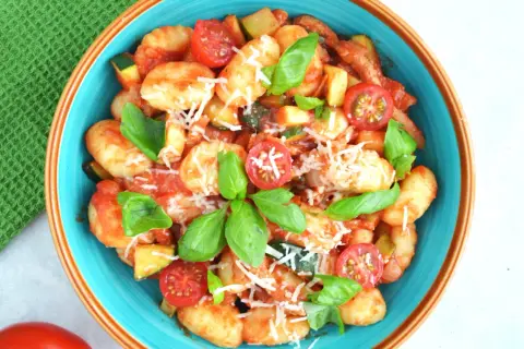 Pyszne gnocchi z sosem pomidorowym, cukinią, pomidorkami koktajlowymi i bazylią, posypane parmezanem.