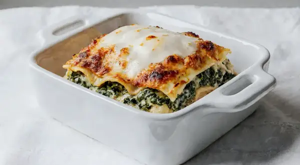 Pyszne lasagne ze szpinakiem w białym naczyniu, zrumienione ciasto i kremowy ser.