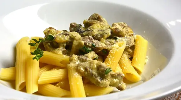 Penne z kremowym sosem i kawałkami wołowiny, posypane parmezanem i udekorowane gałązką ziół. Pyszny makaron z wołowiną.