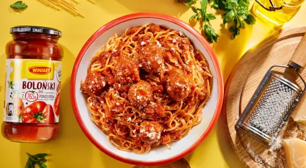 Pyszne spaghetti bolognese z klopsikami w sosie pomidorowym, obok słoik sosu i tarka z parmezanem.