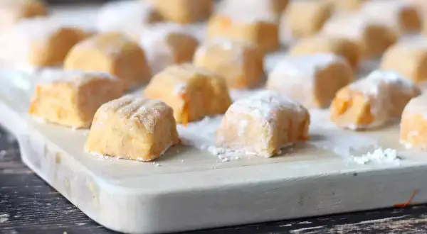 Pomarańczowe gnocchi z dyni, posypane cukrem pudrem, ułożone na desce.