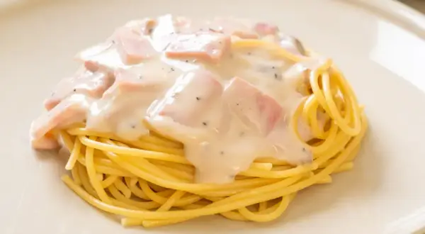 Pyszny makaron z jajkiem i boczkiem w kremowym sosie, posypany pieprzem, podany na białym talerzu.