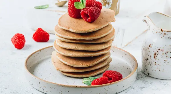 Stos fit pancakes z odżywki białkowej bez banana, udekorowane malinami i miętą, na talerzu.