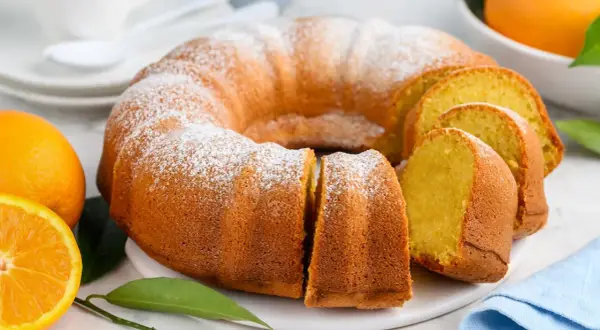 Puszysta babka piaskowa, oprószona cukrem pudrem, z pomarańczami w tle. Idealna na deser.