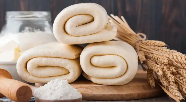 Rolowane ciasto francuskie, choć po terminie, wygląda apetycznie. Obok kłosy zbóż i mąka.