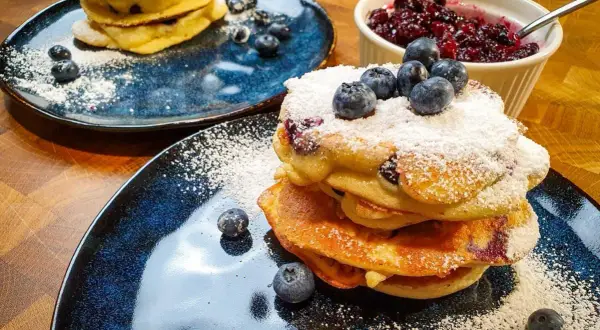 Pyszne pancakes z borówkami, posypane cukrem pudrem i świeżymi owocami. Idealne na śniadanie.
