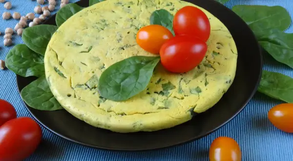 Puszysty omlet z ciecierzycy ze szpinakiem, ozdobiony pomidorkami koktajlowymi i świeżym szpinakiem.