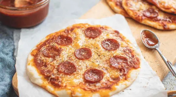 Pyszna pizza z tortilli z pepperoni i serem, obok sos w miseczce i łyżeczka.